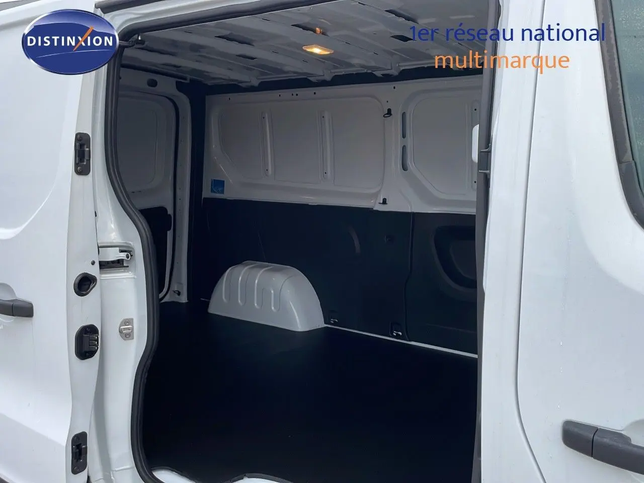 Vue intérieure du fourgon Renault Trafic blanc glacier, montrant l'espace de chargement vide avec porte latérale ouverte.