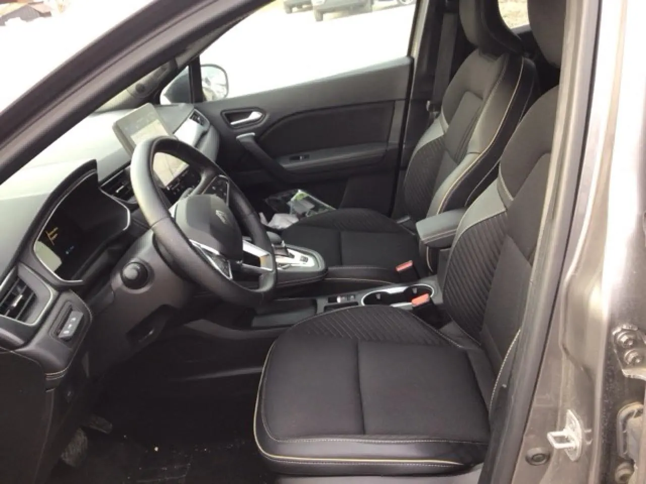 Vue intérieure côté conducteur de la Renault SYMBIOZ gris Cassiopée, sièges noirs avec surpiqûres claires et console centrale moderne.