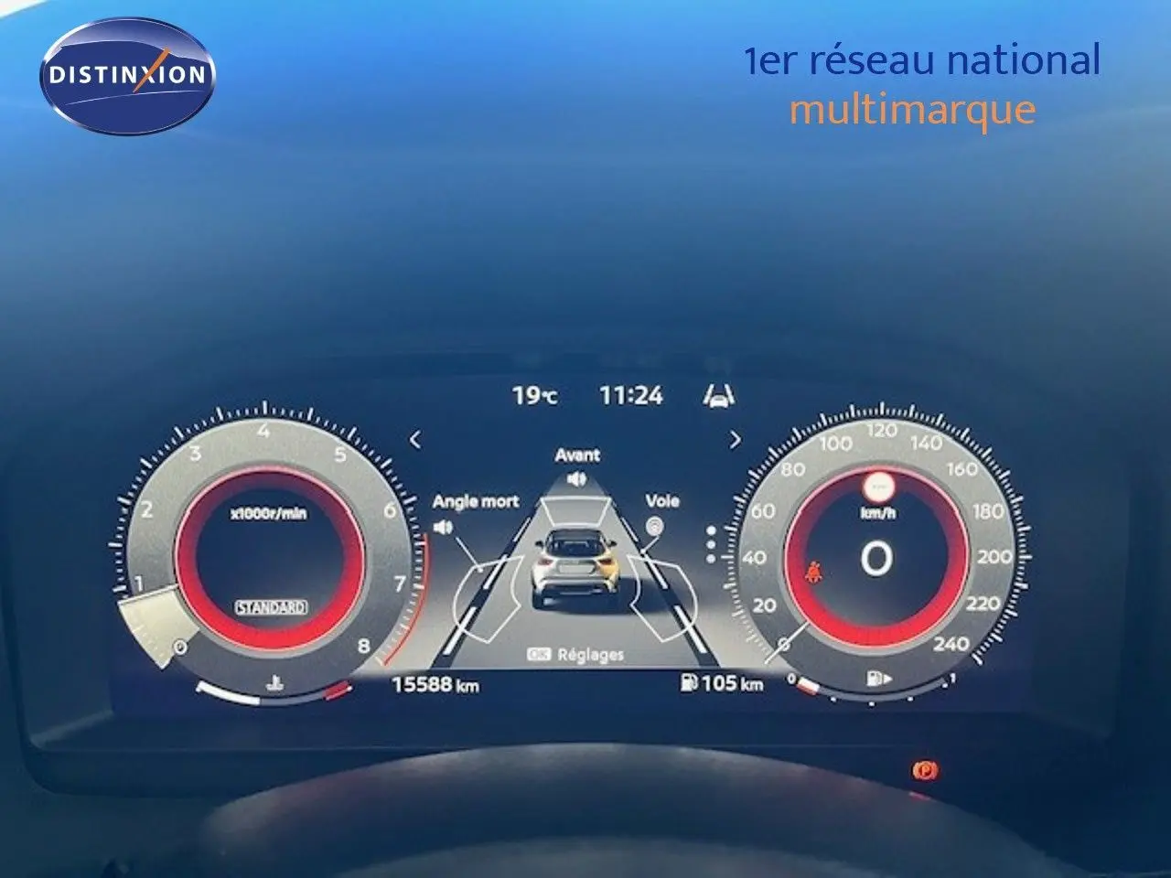 Tableau de bord numérique du Nissan Juke bleu magnétique, affichage central avec alertes d'angle mort et vitesse à zéro.