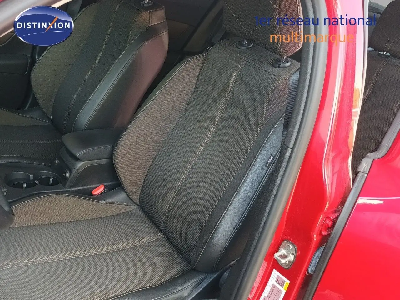 Vue intérieure côté conducteur du siège avant en tissu et cuir, portière ouverte sur carrosserie rouge métallisée.