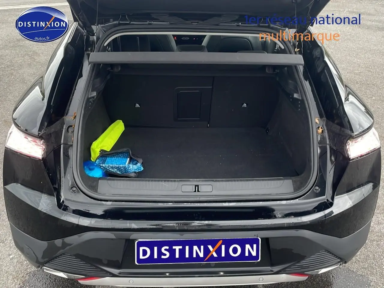 Vue arrière du coffre ouvert d'une DS4 E-tense 225 Cross Trocadero noire avec intérieur spacieux et objets colorés à l'intérieur.