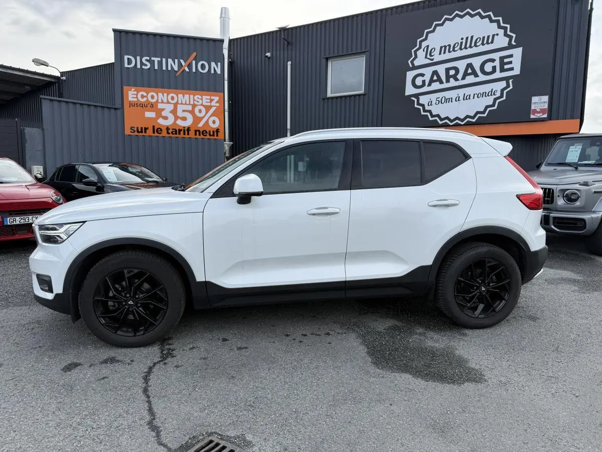 Profil côté gauche d'un Volvo XC40 blanc avec jantes alliage noires, garé devant un garage commercial.
