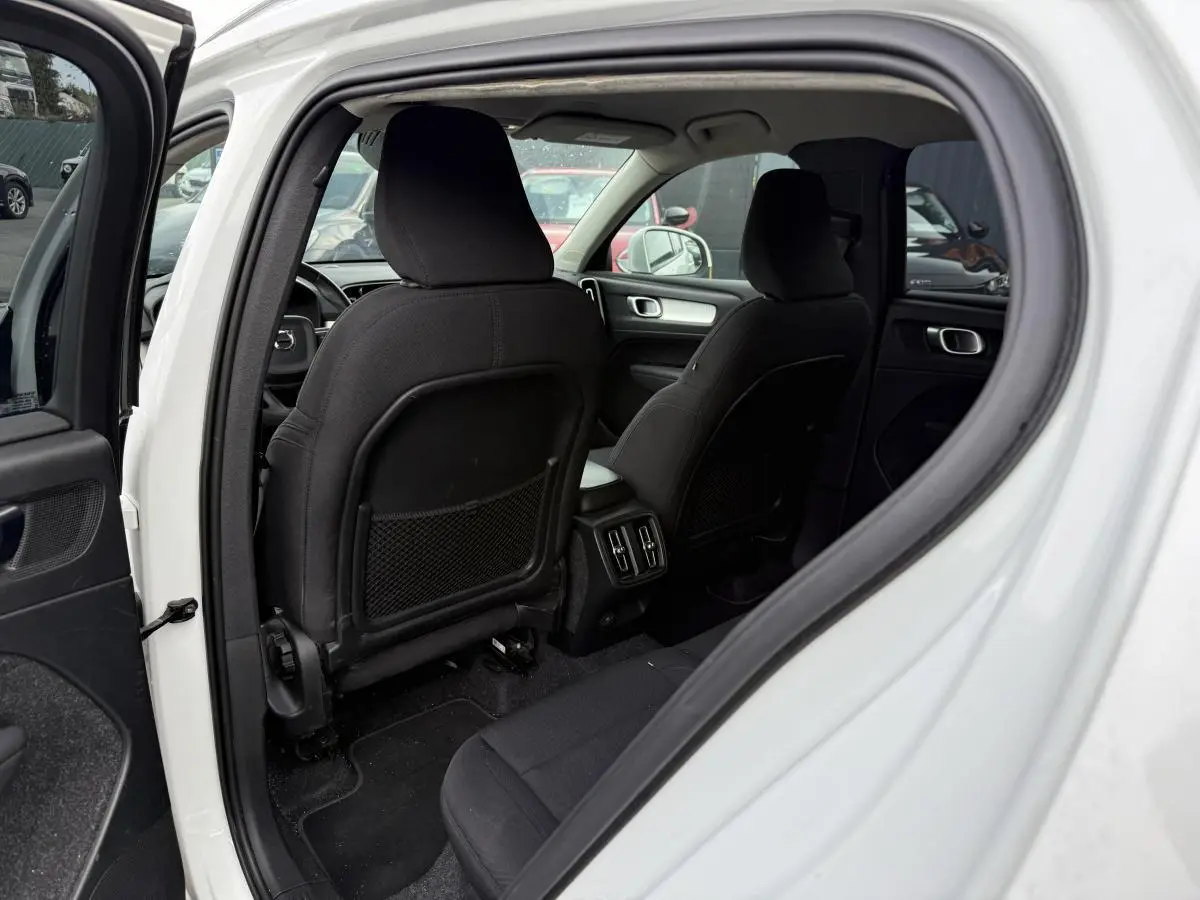 Intérieur arrière du Volvo XC40 blanc 2020, vue côté gauche avec sièges tissu noirs et console centrale visible.