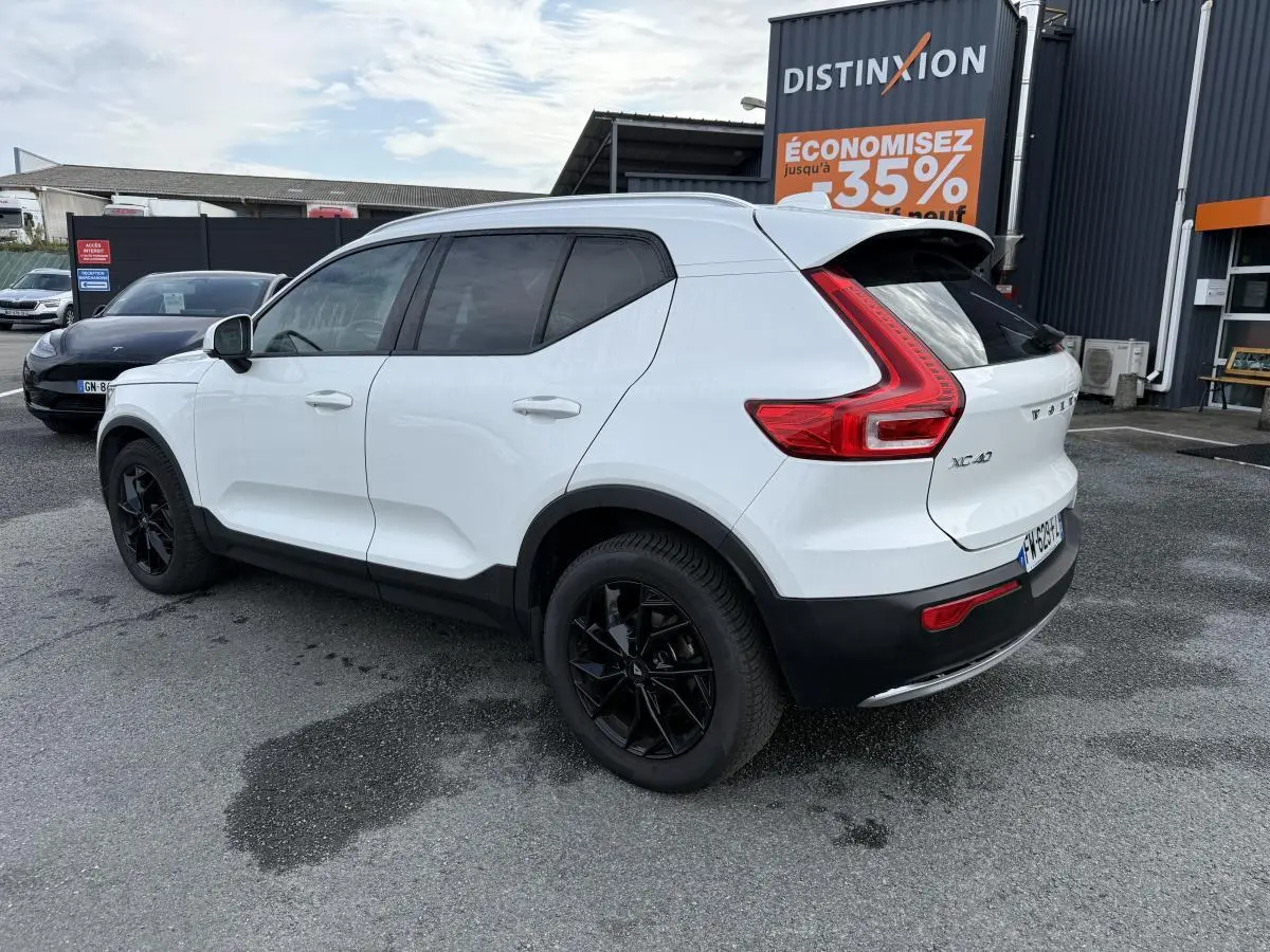 Vue 3/4 arrière droite d'un Volvo XC40 blanc avec jantes alliage noires et protections noires sur passages de roues.