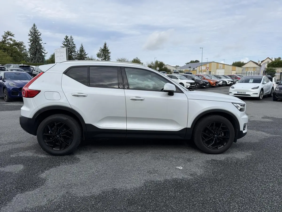 Profil côté gauche d'un Volvo XC40 blanc avec jantes alliage noires 18 pouces sur parking extérieur.