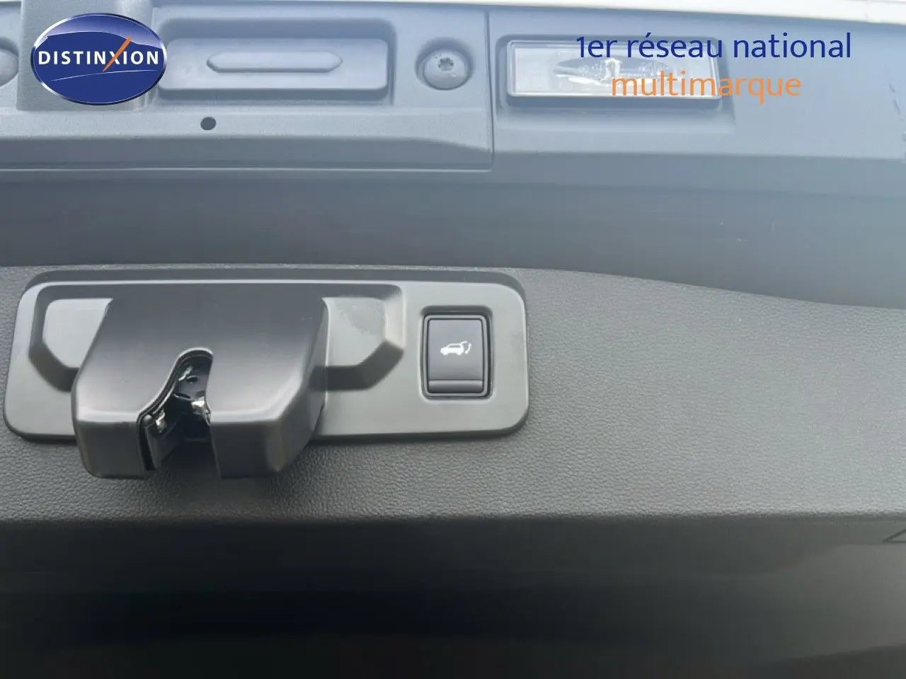 Gros plan sur la serrure et le bouton d'ouverture électrique du hayon d'une Renault Symbioz blanc nacré.