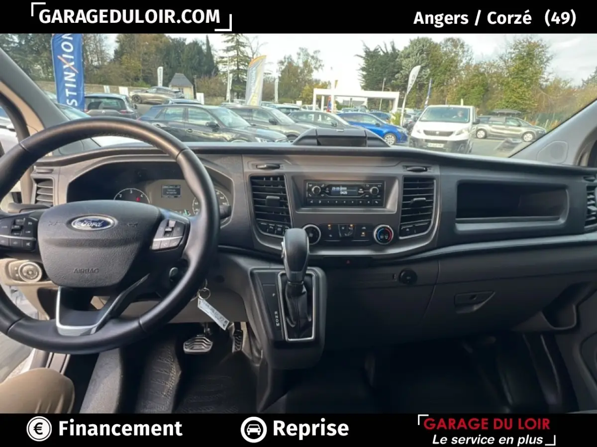 Vue intérieure du tableau de bord et volant noir du Ford Transit Custom Fourgon blanc, avec levier de vitesse automatique visible.