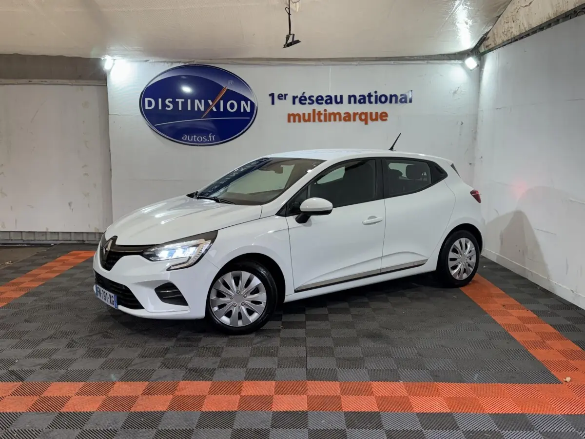 Renault Clio Business TCe 100 blanc vue 3/4 avant droit, phares LED allumés, stationnée en intérieur sur sol damier noir et orange.