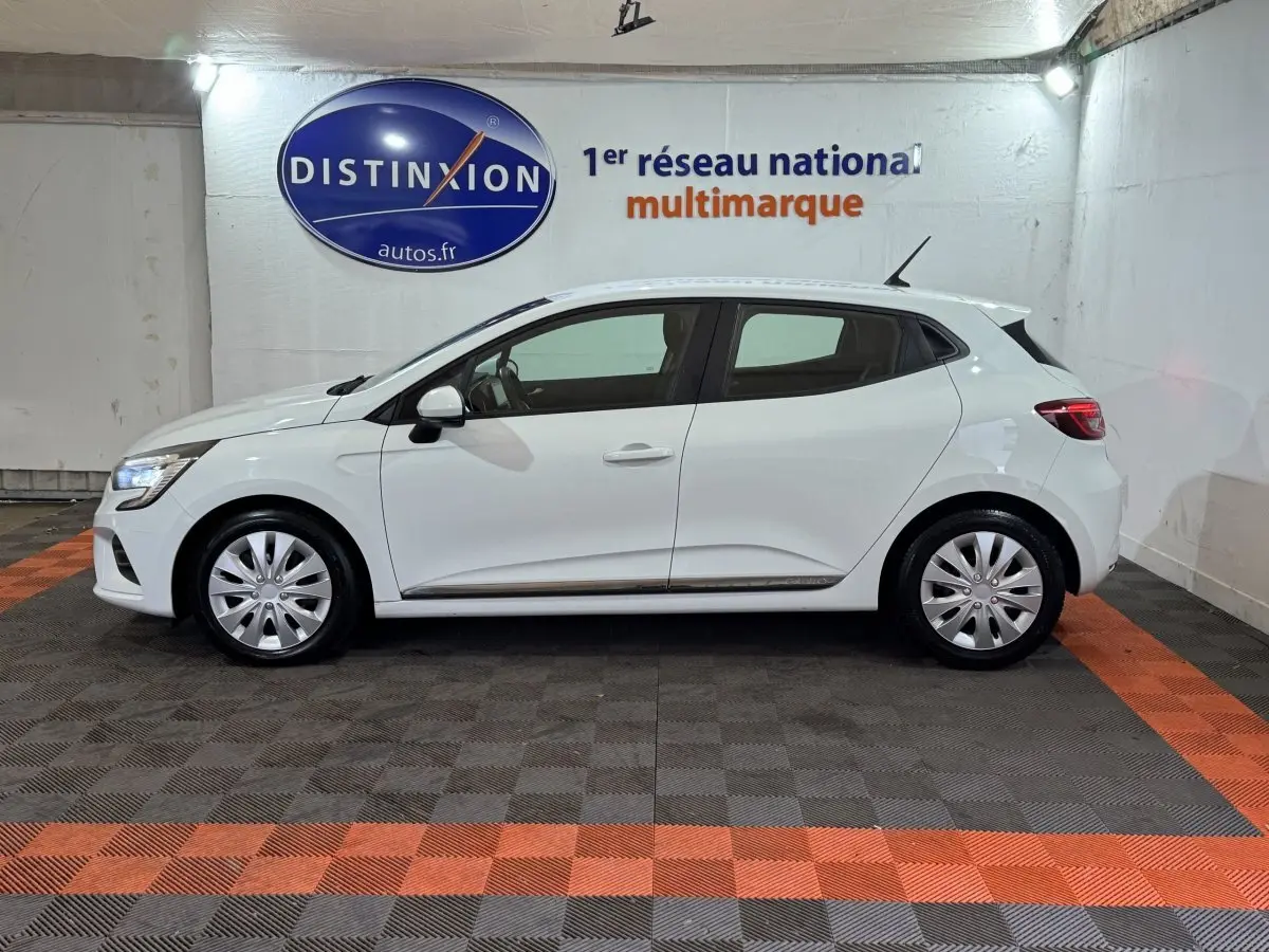 Profil droit d'une Renault Clio Business TCe 100 blanche de 2020, avec jantes acier et feux LED visibles en intérieur showroom.