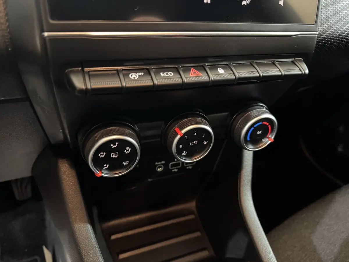 Gros plan sur les commandes de climatisation et boutons de fonction noirs du tableau de bord de la Renault Clio Business blanche.