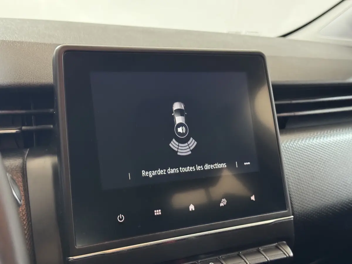 Écran tactile central de la Renault Clio Business blanc, affichant une alerte de détection d'obstacles au stationnement.