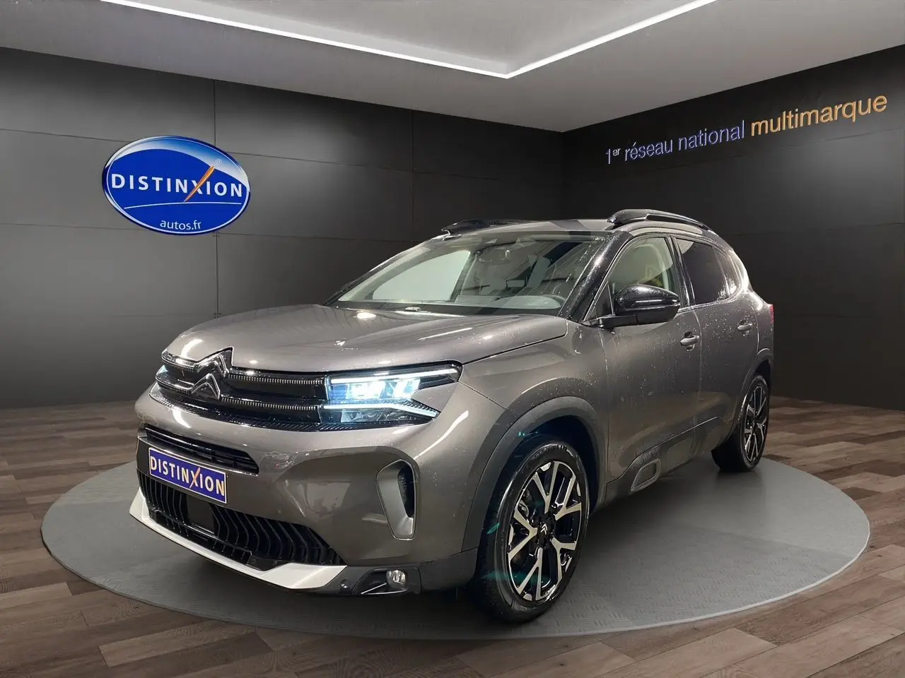 Citroën C5 Aircross gris platinium en 3/4 avant droit avec phares allumés dans un showroom.