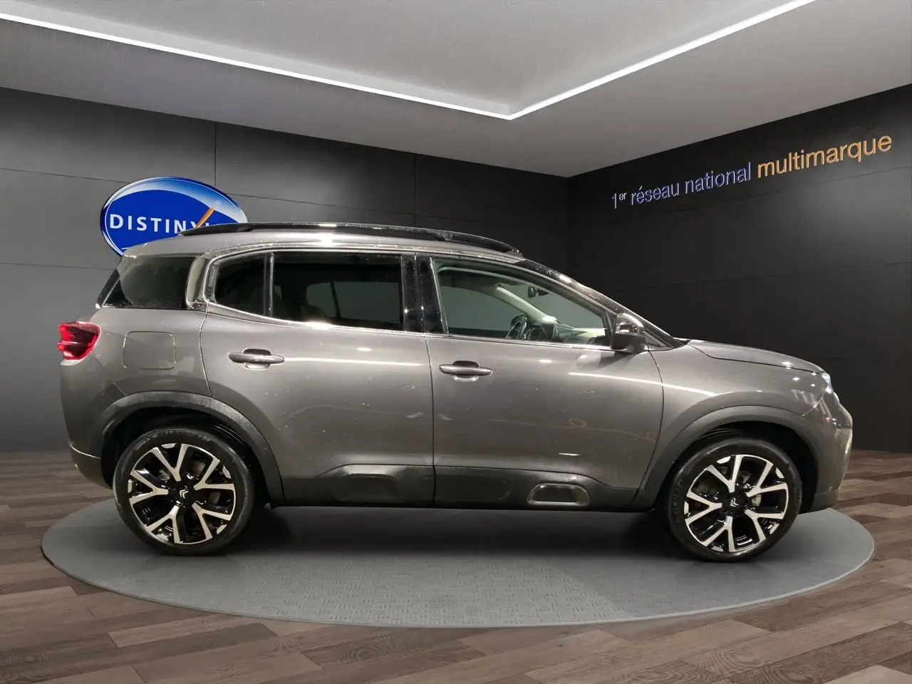 Profil droit d'un SUV Citroën C5 Aircross gris platinium avec jantes alliage noires et toit panoramique en showroom.