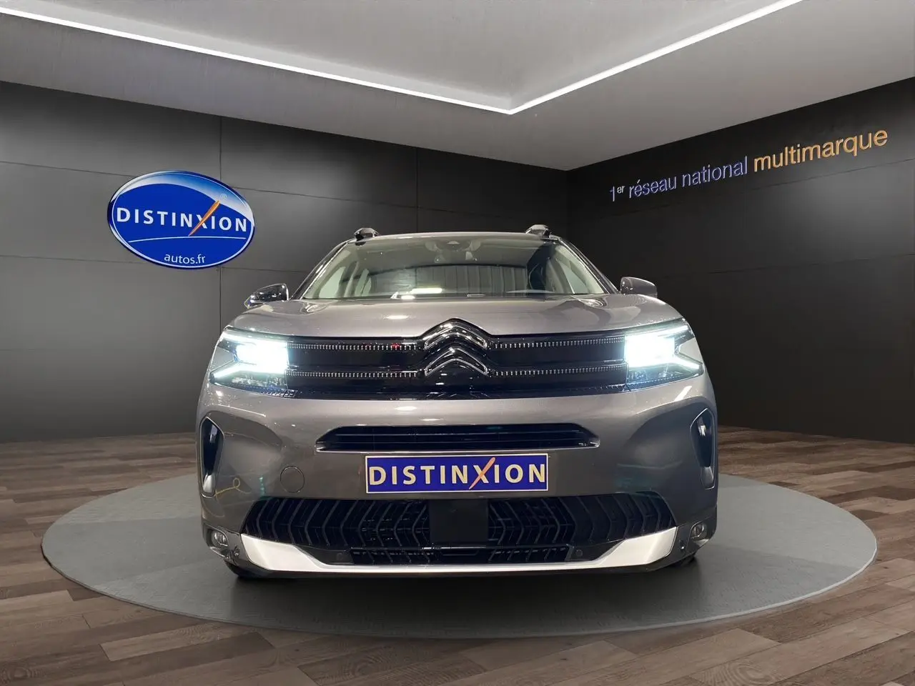Vue frontale d'un Citroën C5 Aircross gris platinium 2023 avec phares LED allumés en showroom.