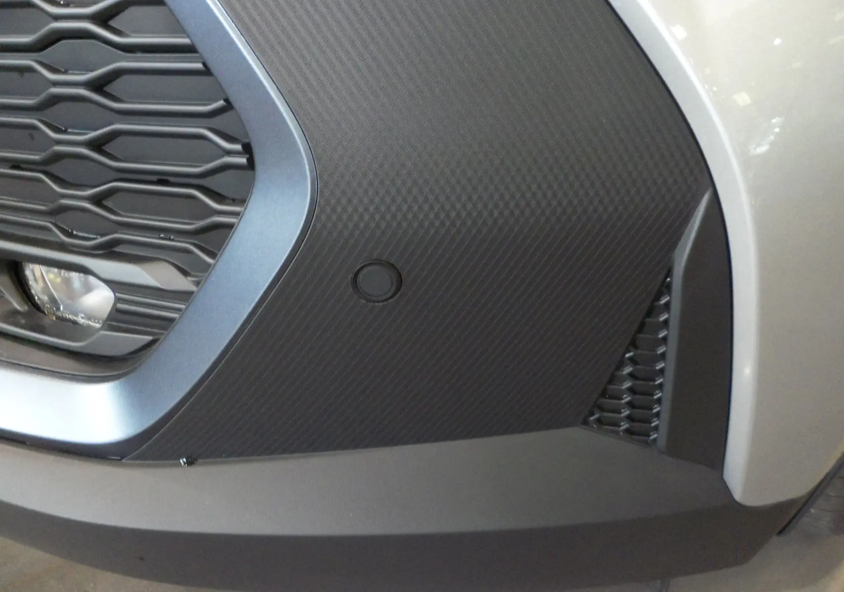 Gros plan sur la calandre avant droite gris minéral du Toyota C-HR Hybride 140 CH Style 2025 avec texture carbone.