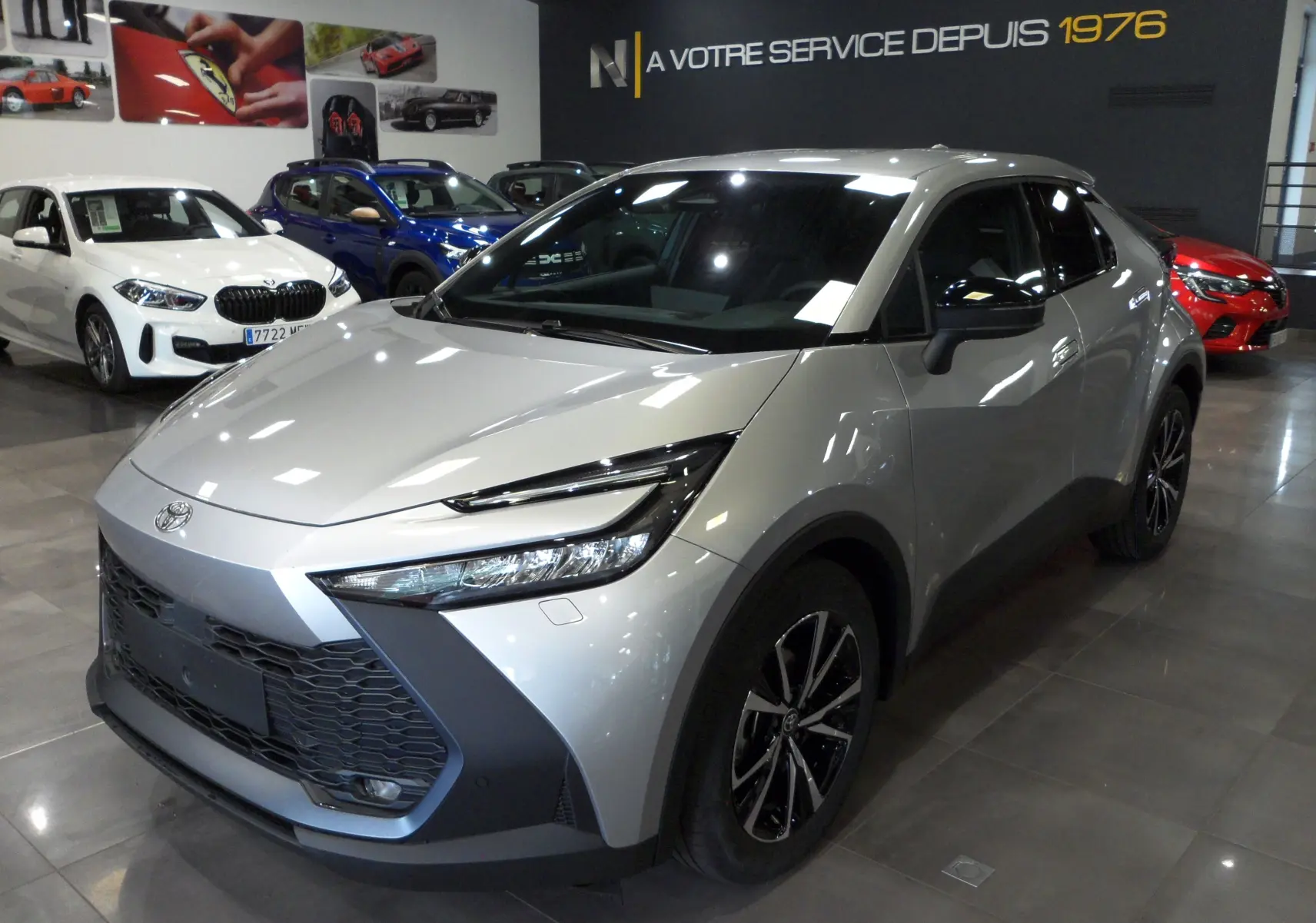 Toyota C-HR hybride gris minéral vu en 3/4 avant droit dans un showroom avec jantes bi-ton noires.