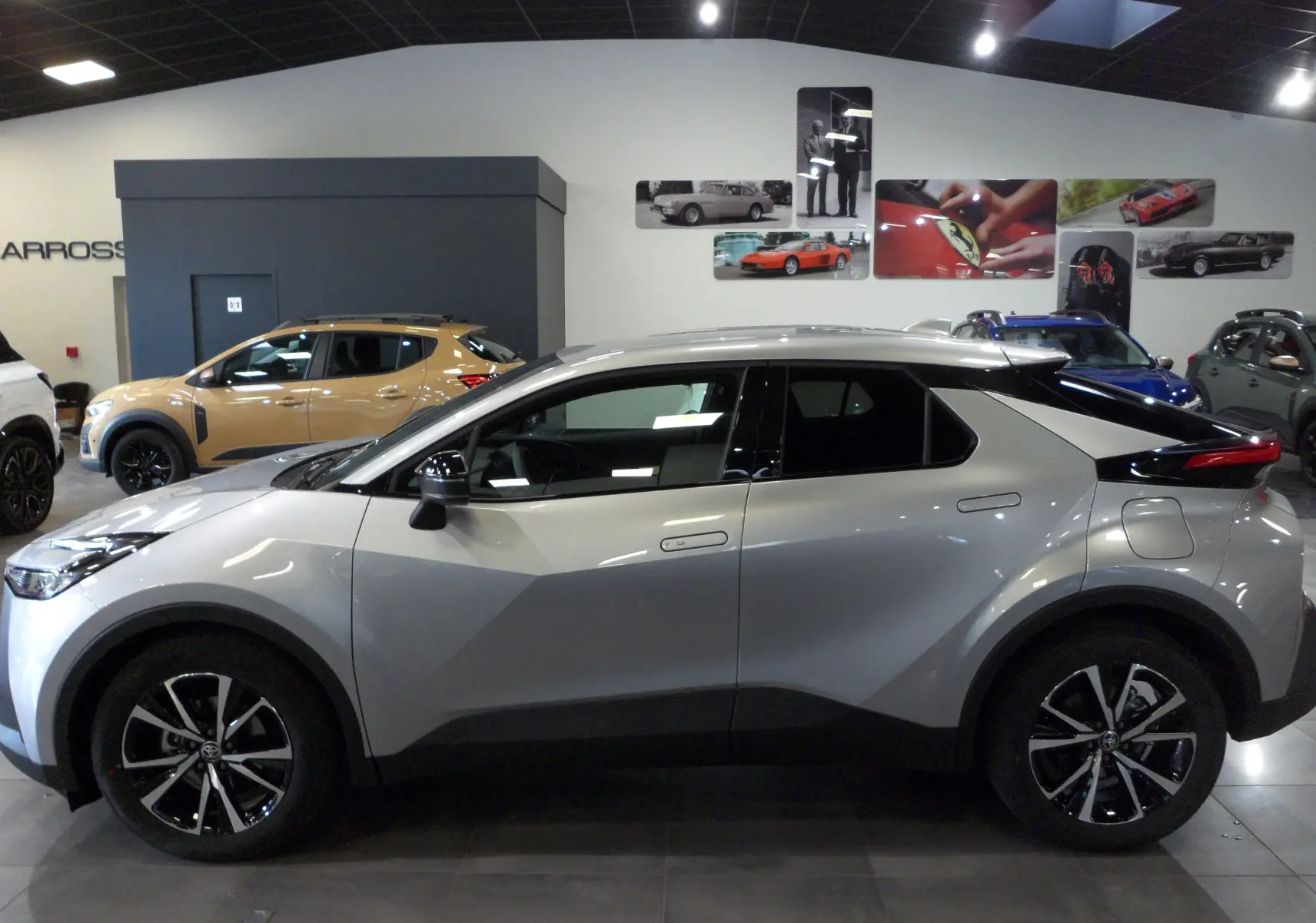 Profil côté gauche du Toyota C-HR hybride 140 ch Style 2025 en gris minéral avec jantes biton visibles en showroom.