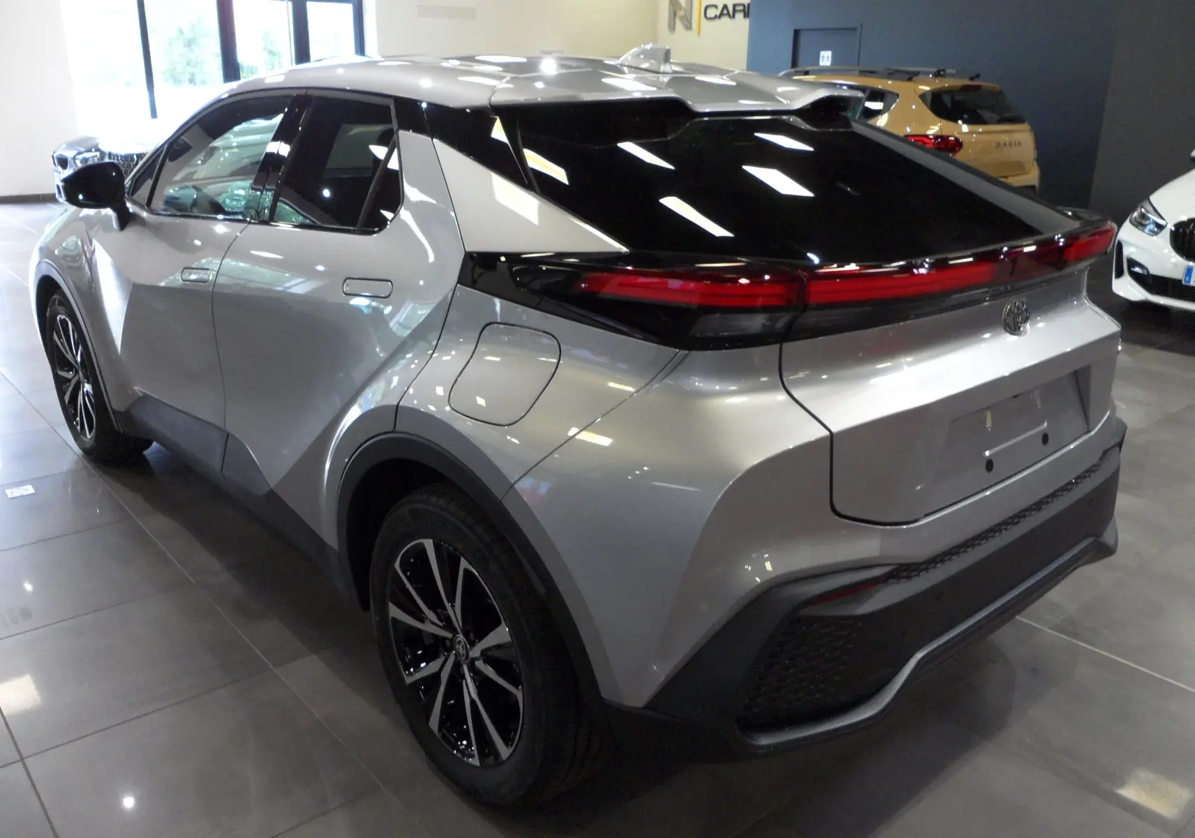 Toyota C-HR hybride gris minéral vu en 3/4 arrière droit, avec toit noir brillant et feux arrière connectés.