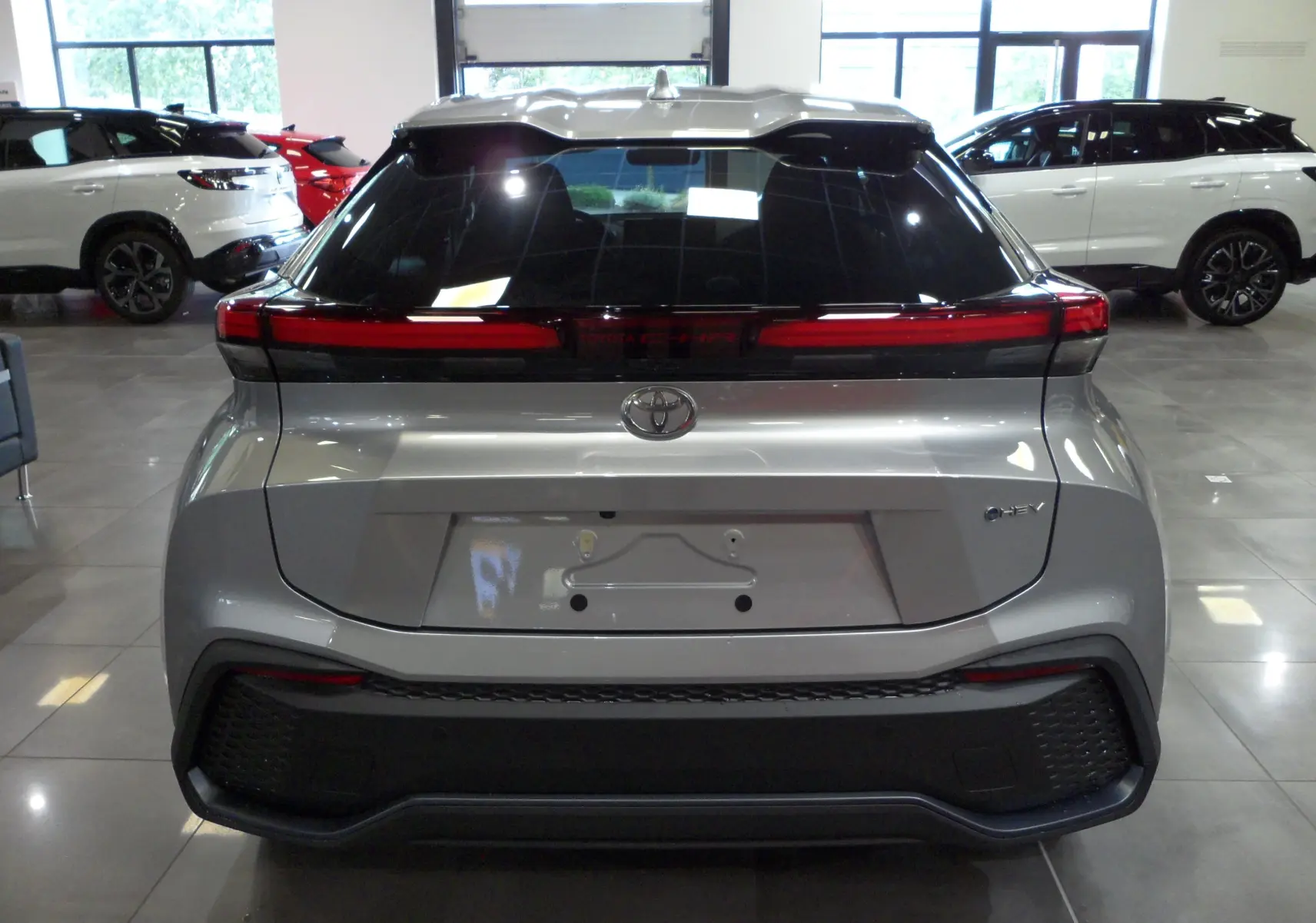 Vue arrière d'un Toyota C-HR hybride 140 ch Style gris minéral avec feux arrière en bandeau lumineux.