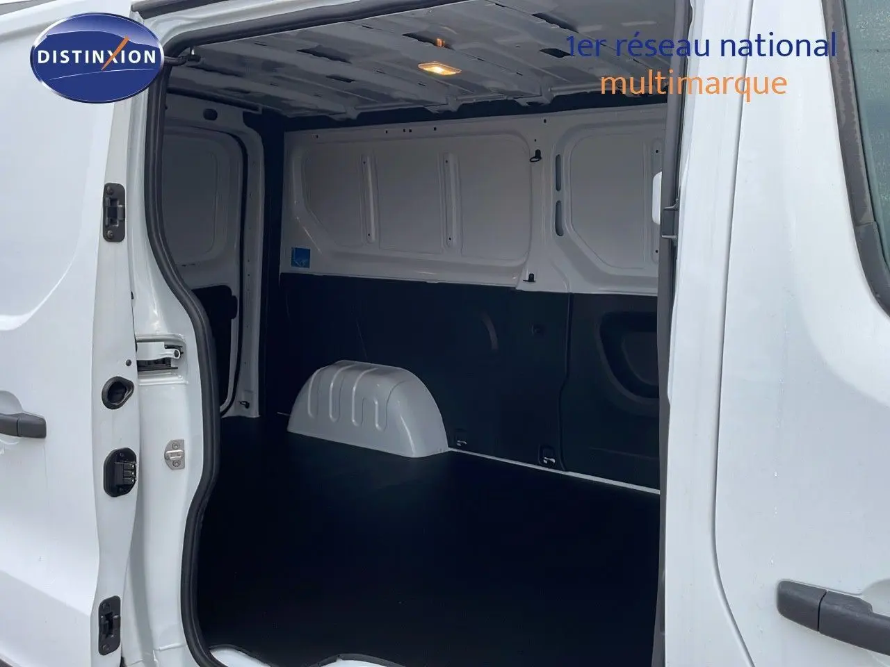 Vue intérieure du fourgon Renault Trafic blanc glacier L2H1, montrant l'espace de chargement vide et les portes latérales ouvertes.