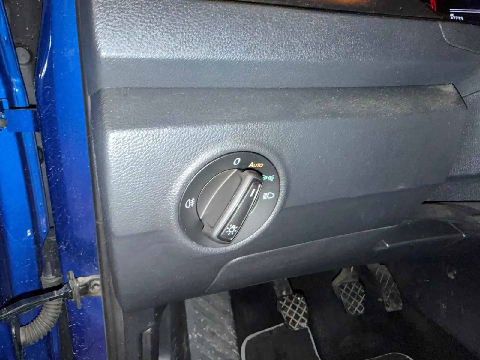 Gros plan sur le tableau de bord côté gauche d’un Volkswagen T-Roc bleu avec commande des phares et pédales de boîte manuelle.