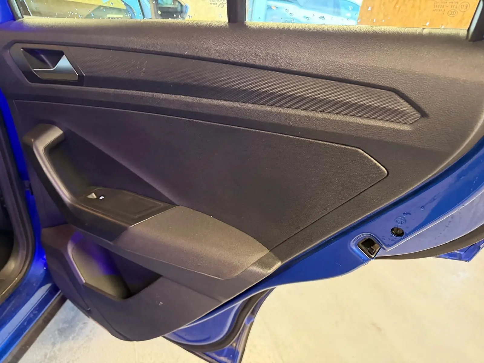 Vue rapprochée de la porte arrière gauche bleu vif du Volkswagen T-Roc 2019 avec panneau intérieur noir et commande de vitre.
