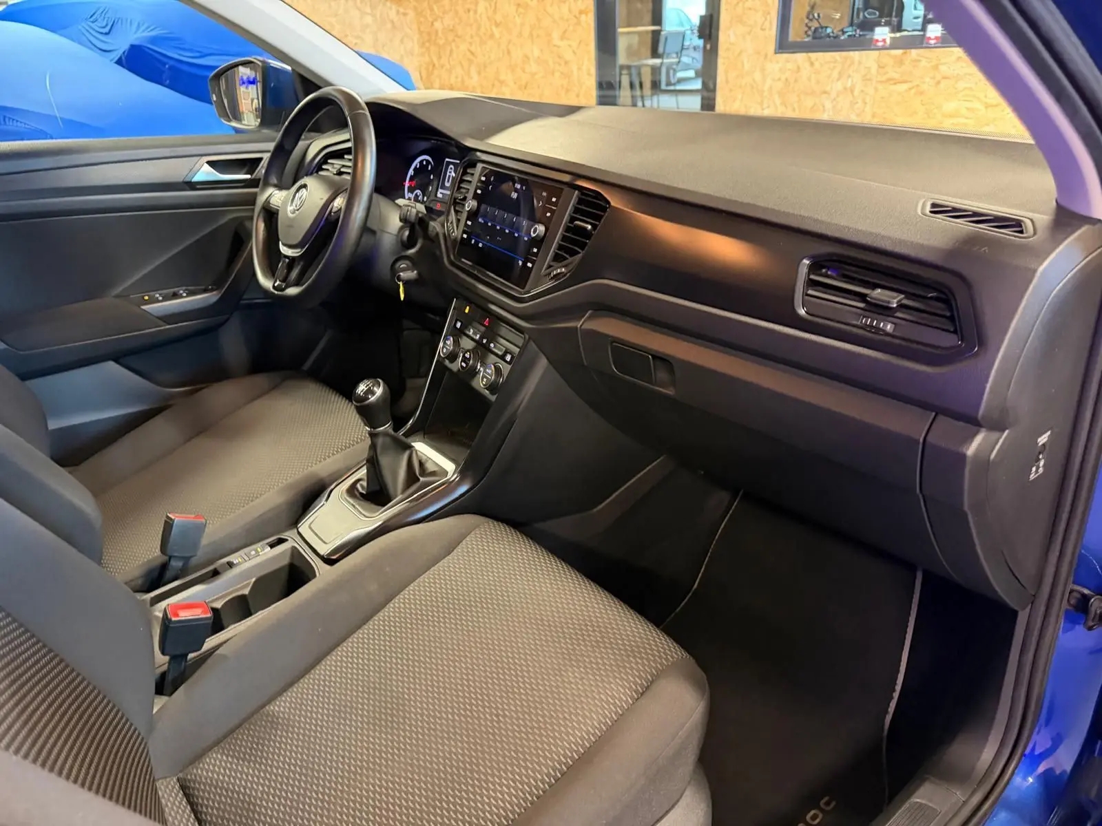 Intérieur avant droit du Volkswagen T-Roc bleu 2019, volant cuir, levier de vitesse manuel et tableau de bord moderne.