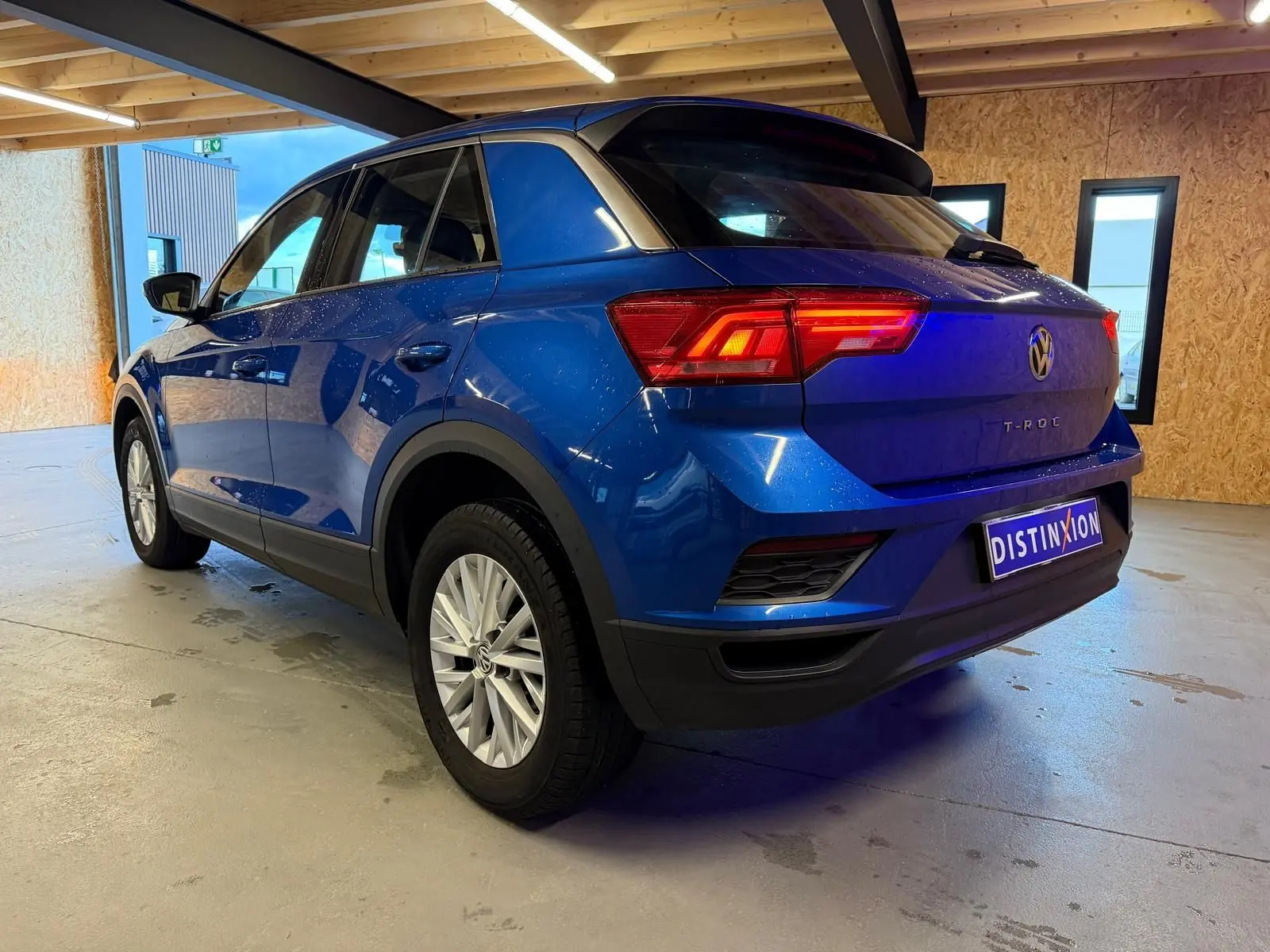 Vue 3/4 arrière droite du Volkswagen T-Roc bleu 2019 avec feux arrière allumés et jantes argentées.