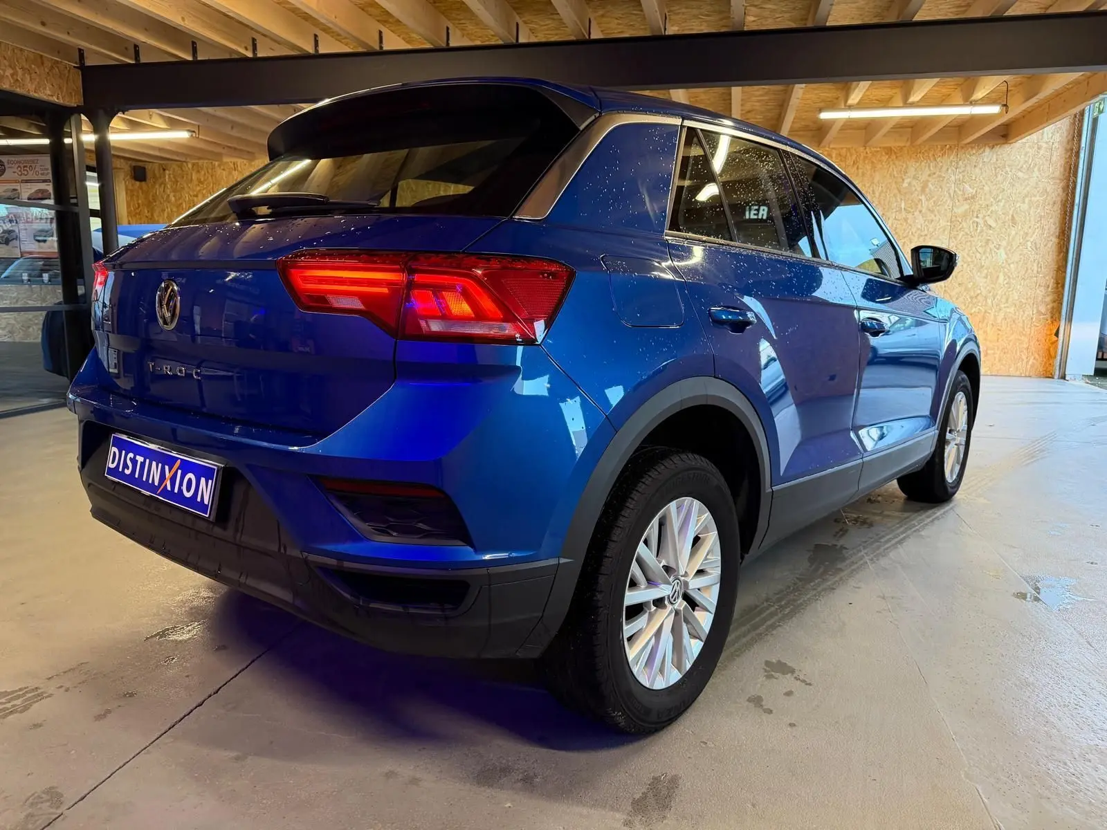 Vue 3/4 arrière droite d'un Volkswagen T-Roc bleu avec feux arrière LED et jantes alliage en intérieur showroom.