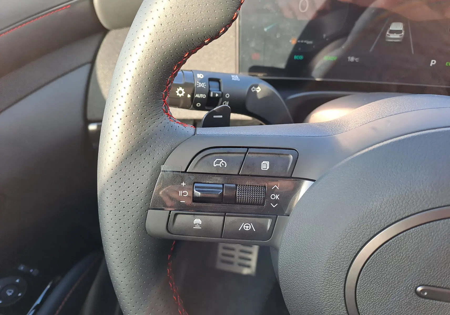 Gros plan sur le volant perforé noir avec surpiqûres rouges du Hyundai Tucson 2025, montrant les commandes multifonctions côté gauche.