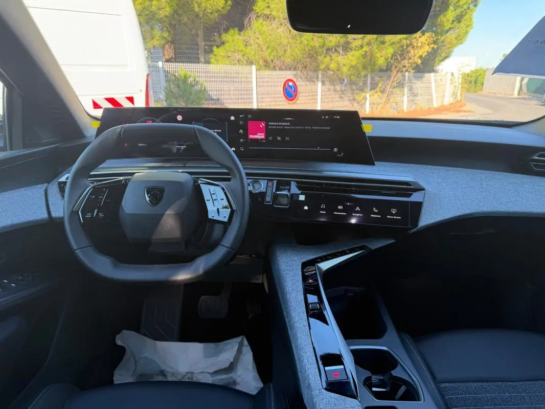 Vue intérieure du tableau de bord et volant du Peugeot 3008 Hybrid 145 e-DCS6 Allure 2025 avec finition tissu bleu et écrans numériques.