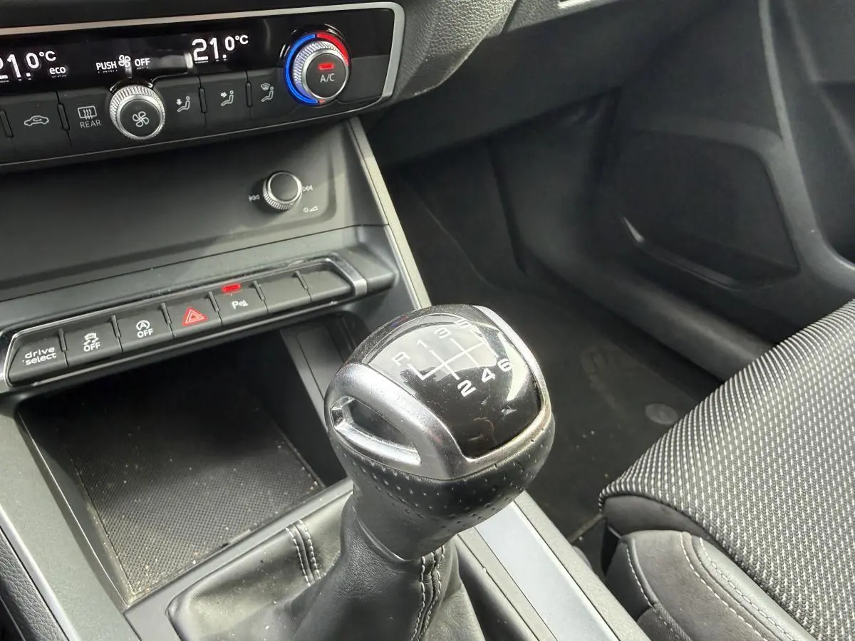 Le levier de vitesses manuel noir de l'Audi Q3 S Line 2019 avec commandes de climatisation en arrière-plan.