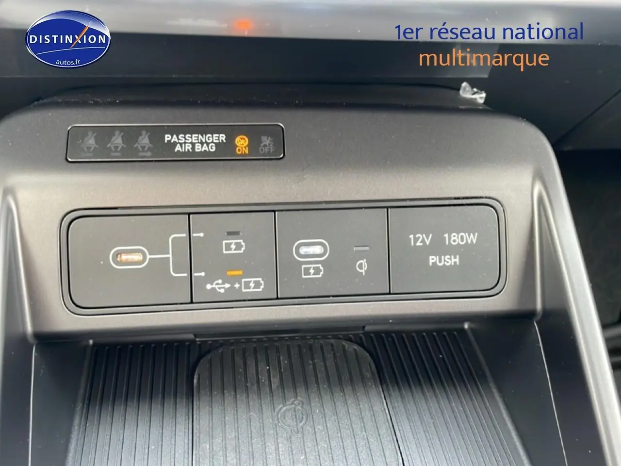 Vue rapprochée du panneau de commandes USB, prise 12V et indication airbag passager du Hyundai Kona bleu 2025.