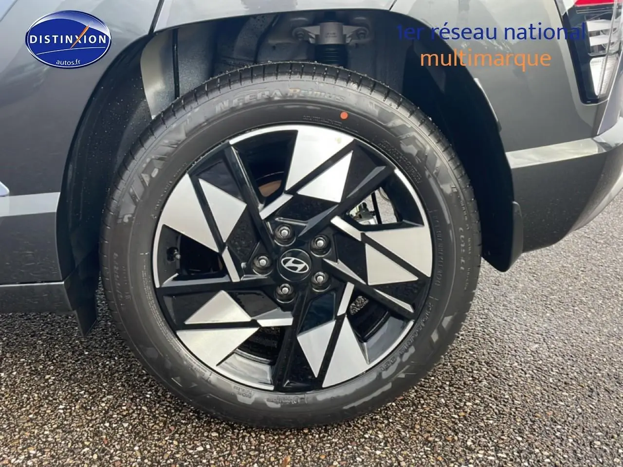 Gros plan sur la roue avant droite avec jante alliage noire et argentée du Hyundai Kona bleu 2025.