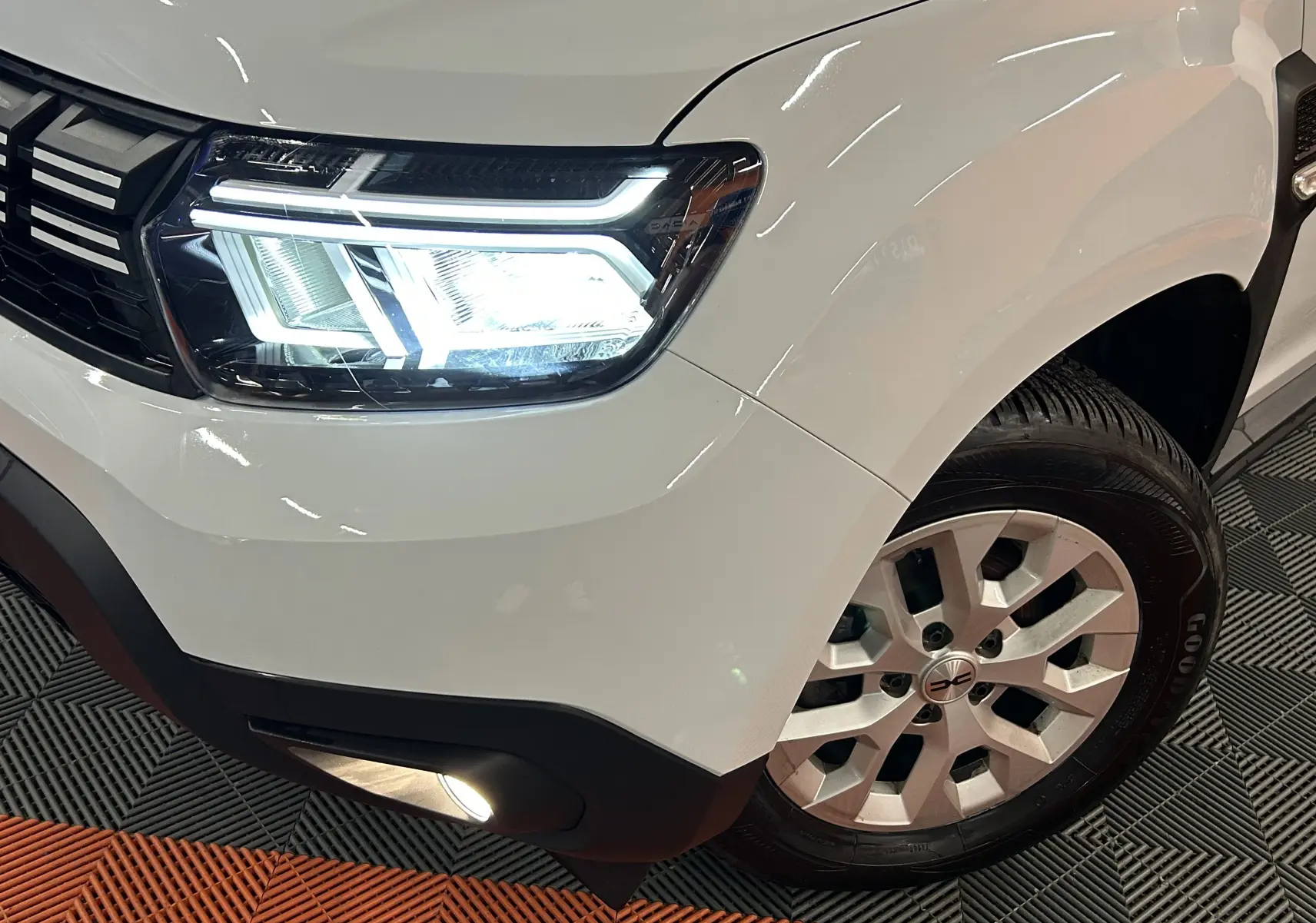 Gros plan sur l'avant droit du Dacia Duster blanc 2023, mettant en valeur le phare LED et la roue avec jante alu.