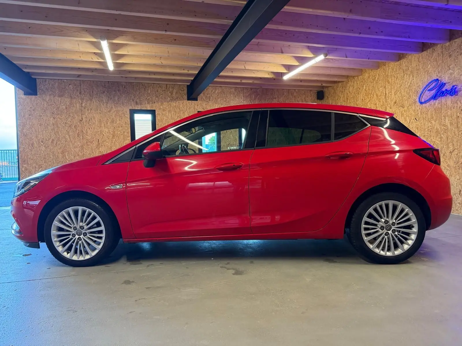 Opel Astra 1.4i Turbo rouge vue de profil côté gauche, avec jantes alu et rétroviseurs électriques rabattables.