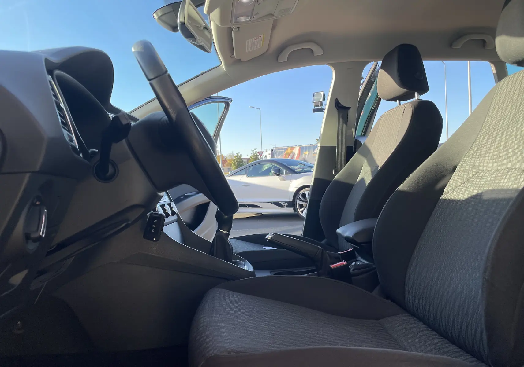 Intérieur côté conducteur d'une SEAT LEON ST gris 2013, sièges tissu gris-noir et volant avec boîte manuelle visible.