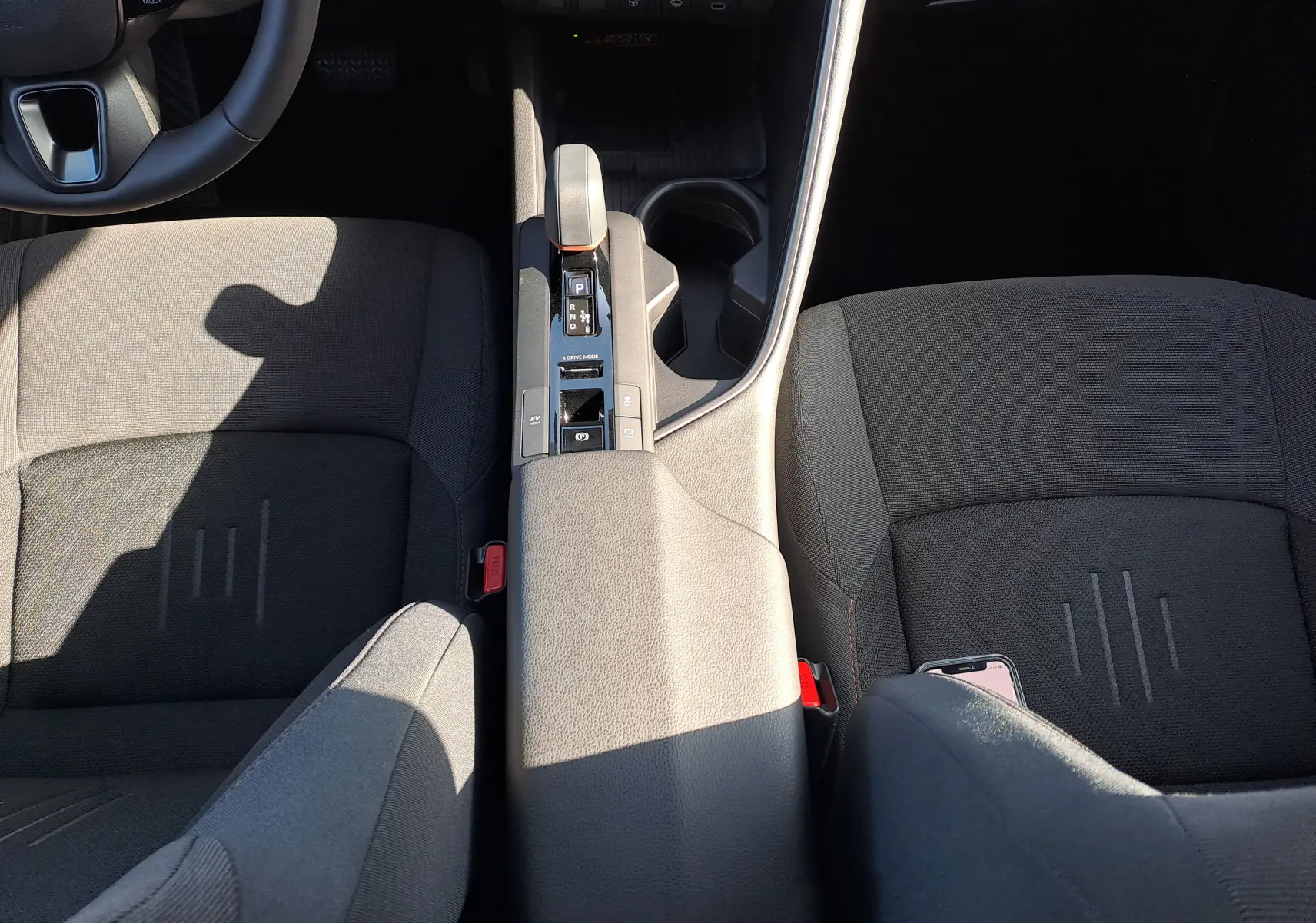 Vue plongeante sur l'intérieur du Toyota C-HR gris minéral, montrant la console centrale et les sièges avant en tissu noir.