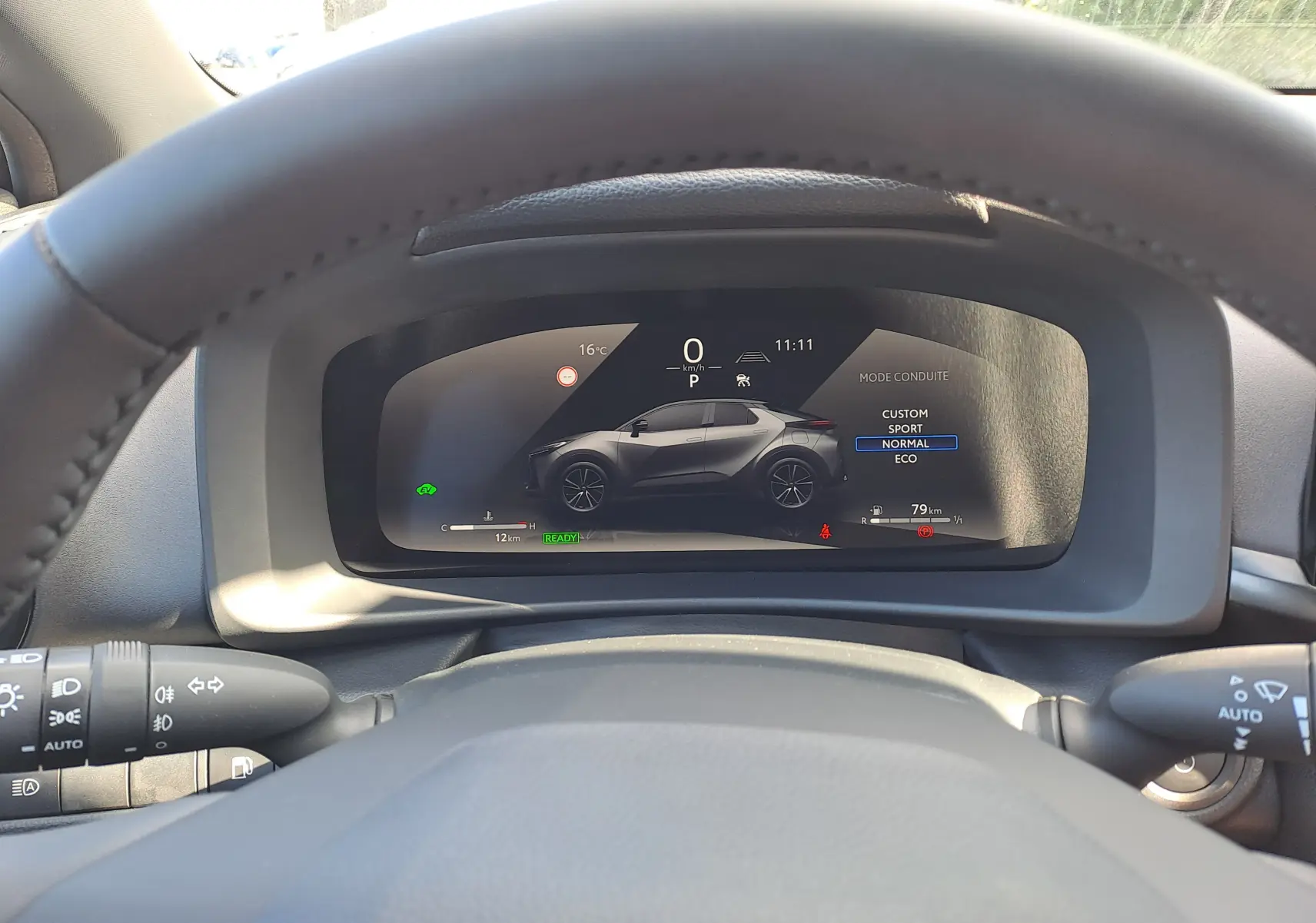 Vue du tableau de bord numérique du Toyota C-HR gris minéral 2025, affichant le mode de conduite et l'autonomie restante.