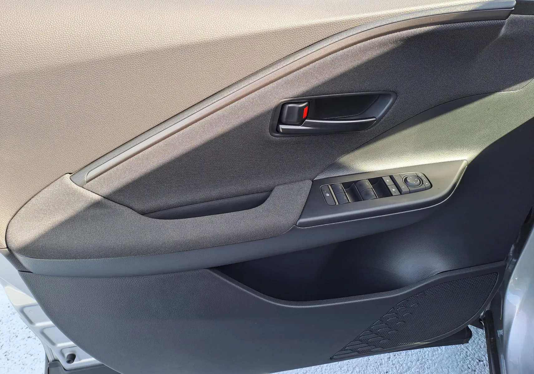 Panneau intérieur côté gauche de porte avant du Toyota C-HR gris minéral, avec commandes de vitres et poignée noire.