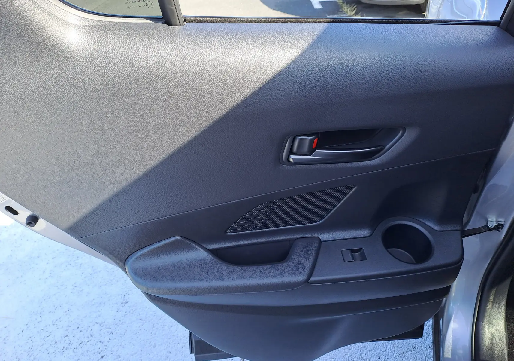 Vue rapprochée de la porte arrière droite grise minéral du Toyota C-HR 2025, avec poignée intérieure et porte-gobelet intégré.