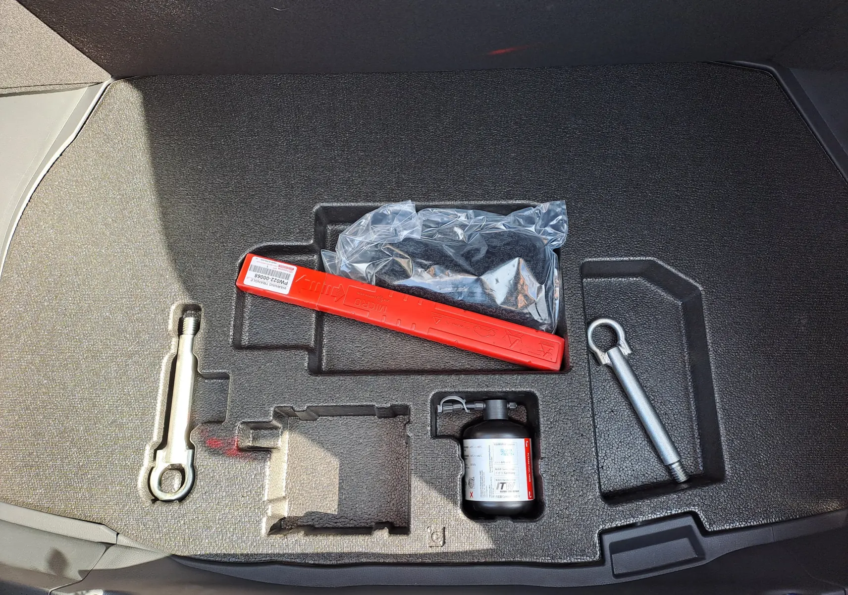 Coffre ouvert du Toyota C-HR gris minéral 2025 montrant le kit de réparation et les outils de secours rangés.