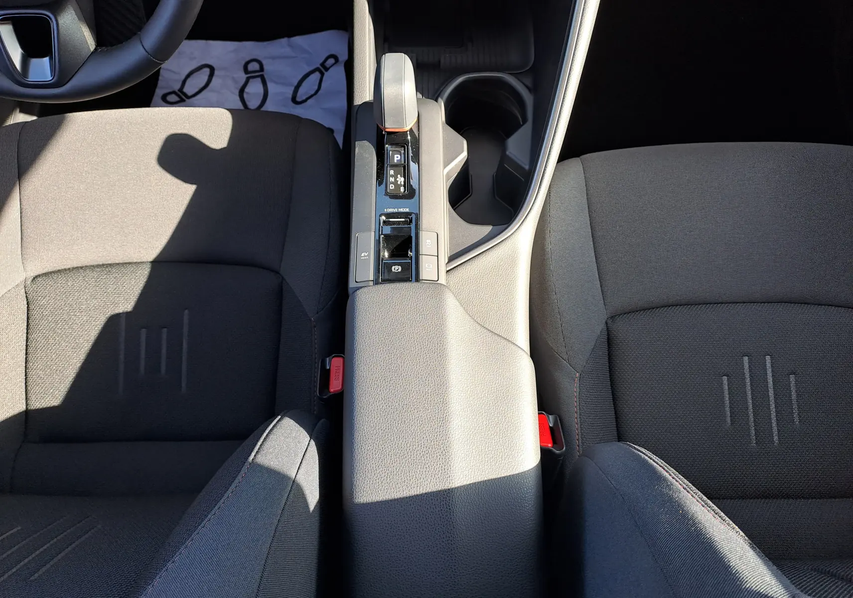 Vue plongeante sur la console centrale et les sièges avant noirs du Toyota C-HR gris minéral 2025 hybride avec boîte auto.