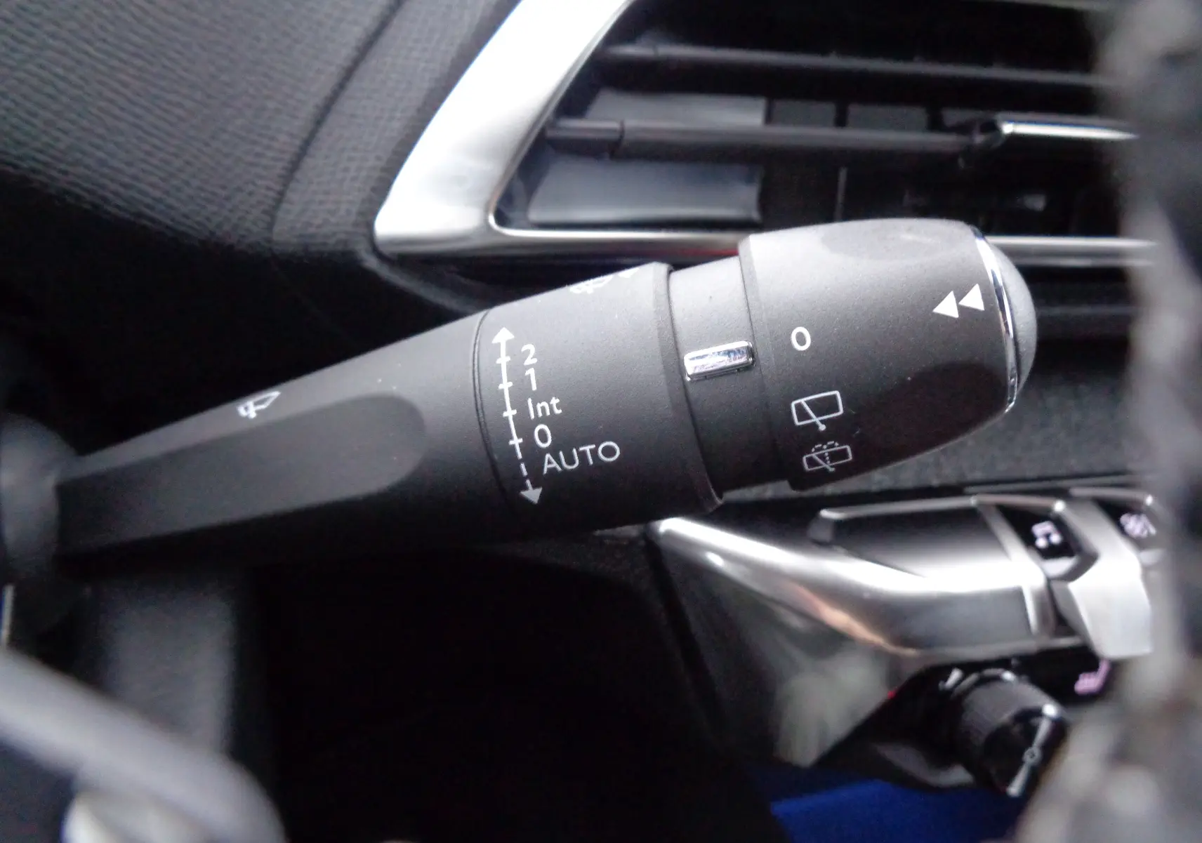 Gros plan sur la commande d'essuie-glace à gauche du volant dans l'habitacle noir du Peugeot 3008 2023.