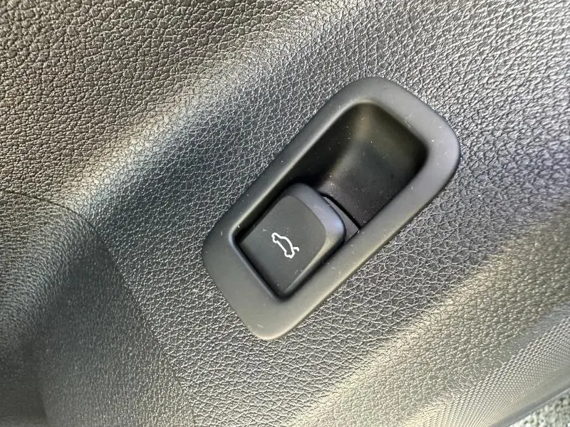 Bouton d'ouverture du coffre en plastique noir sur panneau intérieur texturé d'un Audi Q2 35 TFSI 2023 Noir Mythic métallisé.