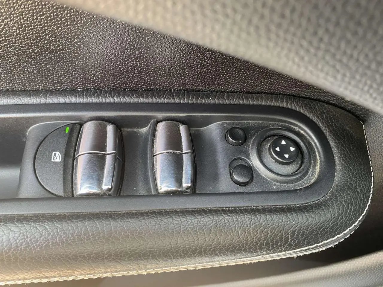 Gros plan sur les commandes des lève-vitres et réglages des rétroviseurs côté conducteur en cuir noir du MINI Countryman gris clair.