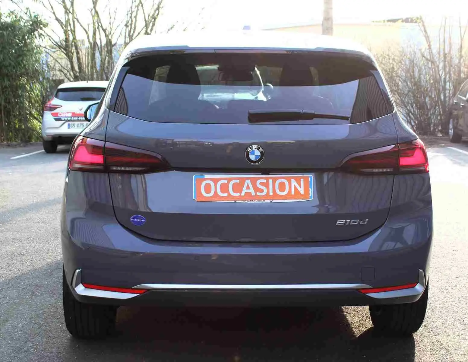 Vue arrière d'une BMW Série 2 Active Tourer gris Nardo métallisé avec feux arrière allumés et plaque "OCCASION" visible.
