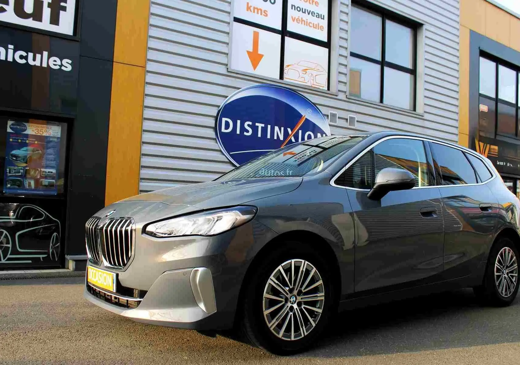 BMW Série 2 Active Tourer gris Nardo métal vue 3/4 avant droit devant un bâtiment commercial.