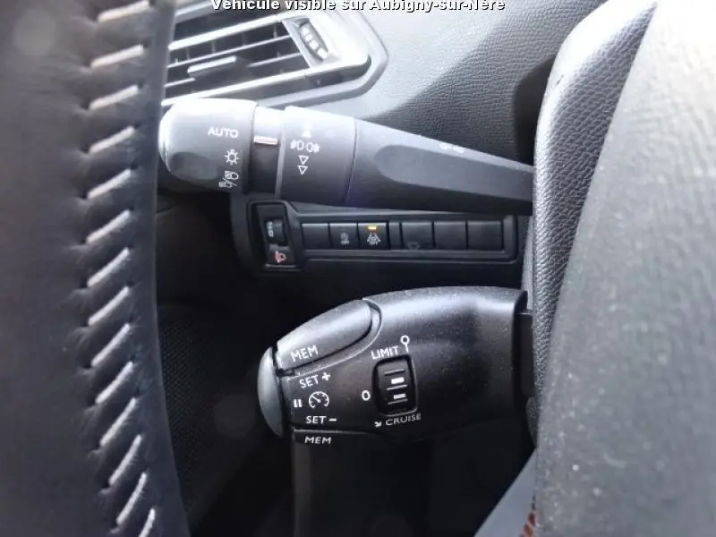 Gros plan sur les commandes de régulateur et feux à gauche du volant d'une Peugeot 308 SW noire de 2018.