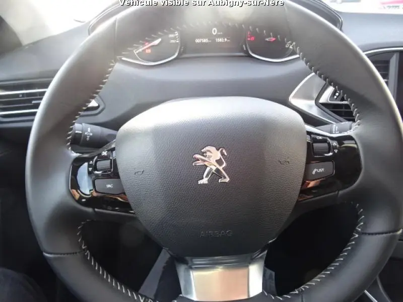 Vue rapprochée du volant cuir noir avec logo Peugeot au centre du poste de pilotage d'une 308 SW noire de 2018.